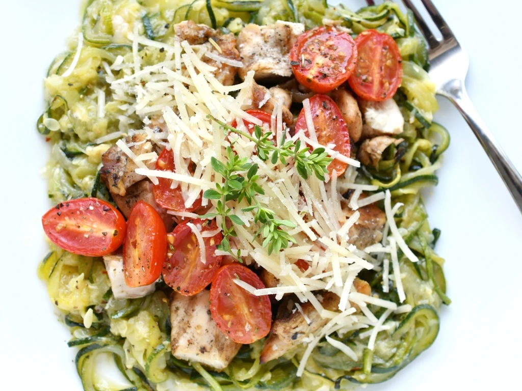 Pesto chicken pasta with spinach, cherry tomatoes, zucchini, and parmesan served with a fork