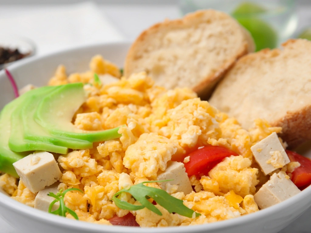 Bowl of tofu and egg scramble with peppers, tomato, avocado, and sourdough toast