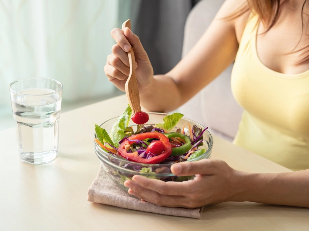 Woman eating a bowl of vegetable salad