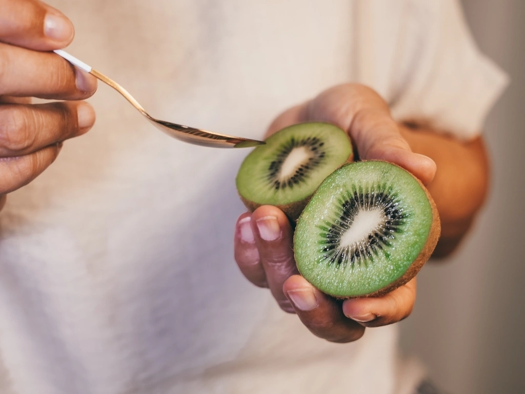 Woman holding sliced kiwi in one hand and a spoon in the other