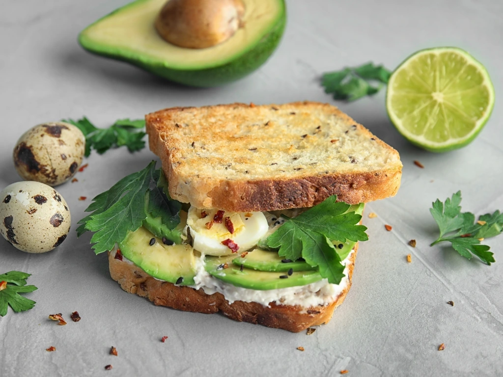Avocado sandwich with sliced avocado, egg, and fresh herbs on toasted bread