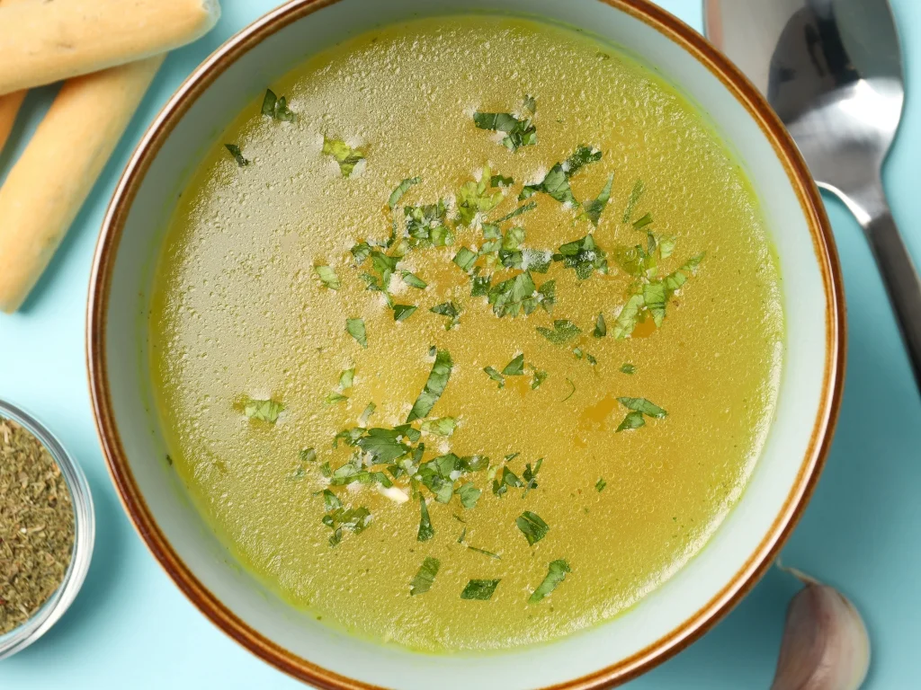 Bowl of clear broth soup topped with chopped herbs