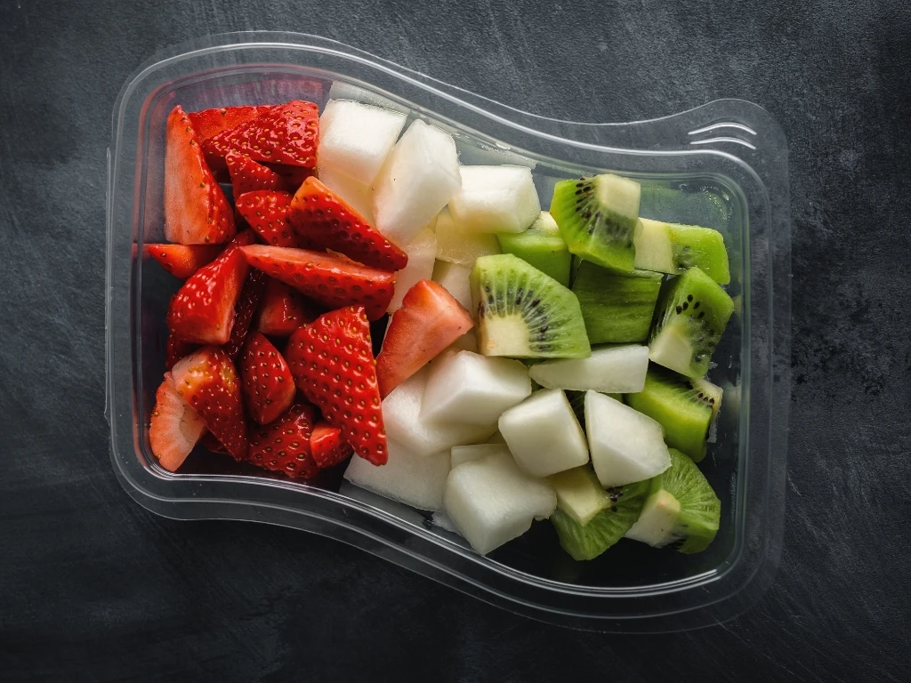 Container of sliced fresh fruit including strawberries, kiwi, and melon pieces