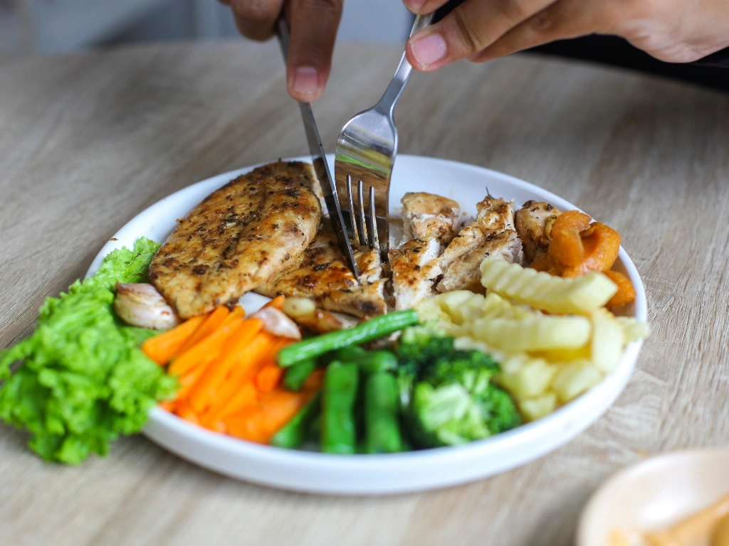Person eating a balanced plate with lean protein and a variety of vegetables