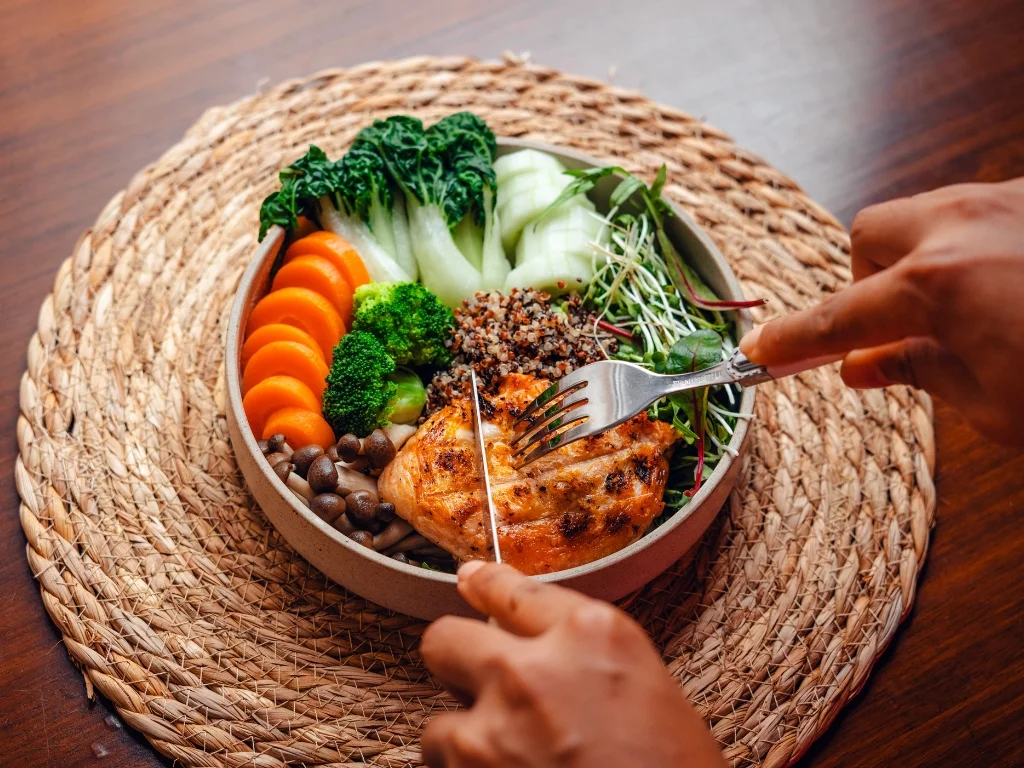 Bowl of grilled chicken breast with quinoa, broccoli, sliced carrots, mushrooms, and bok choy