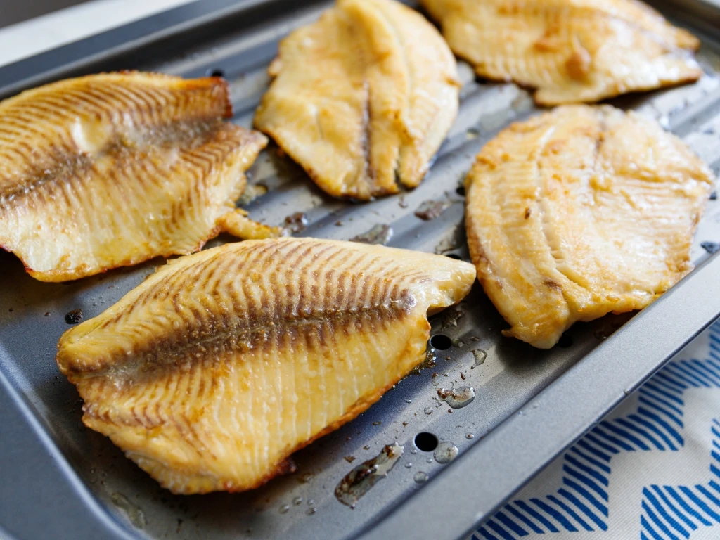 Five seasoned, oven-baked white fish fillets arranged on a dark metal baking sheet