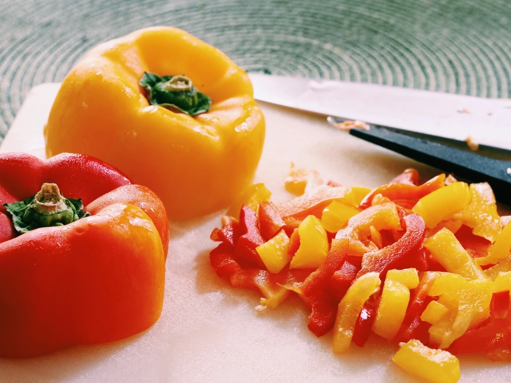 Sliced red and yellow bell peppers on a wooden board, next to a kitchen knife