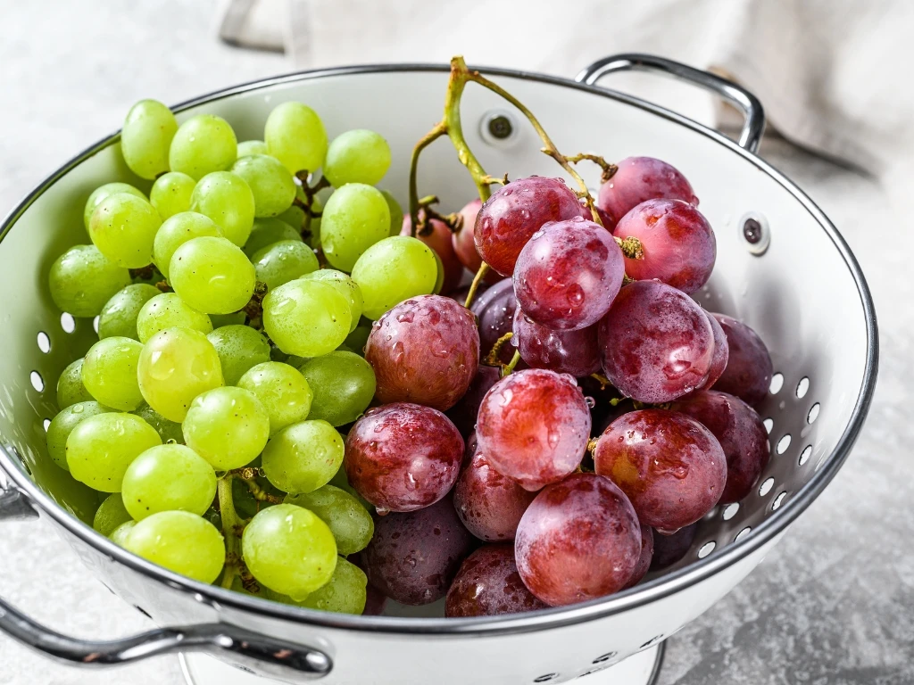 White colander filled with clusters of fresh, newly washed green and red grapes