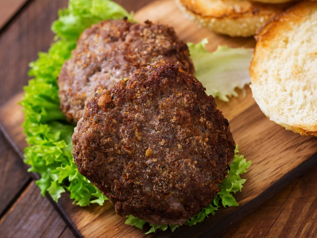Two burger patties served on lettuce next to toasted buns