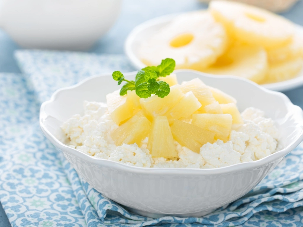 Bowl of cottage cheese with pineapple chunks garnished with microgreens, served next to a plate of more pineapples
