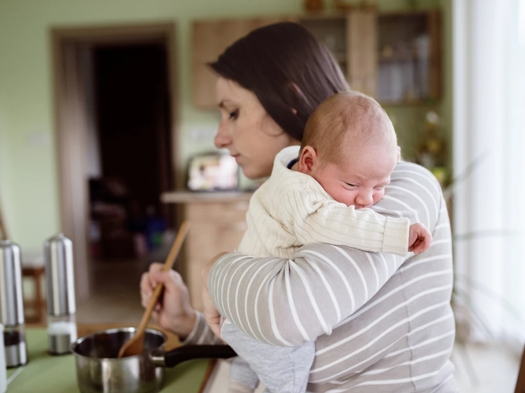 Young mother in kitchen holding baby son, cooking