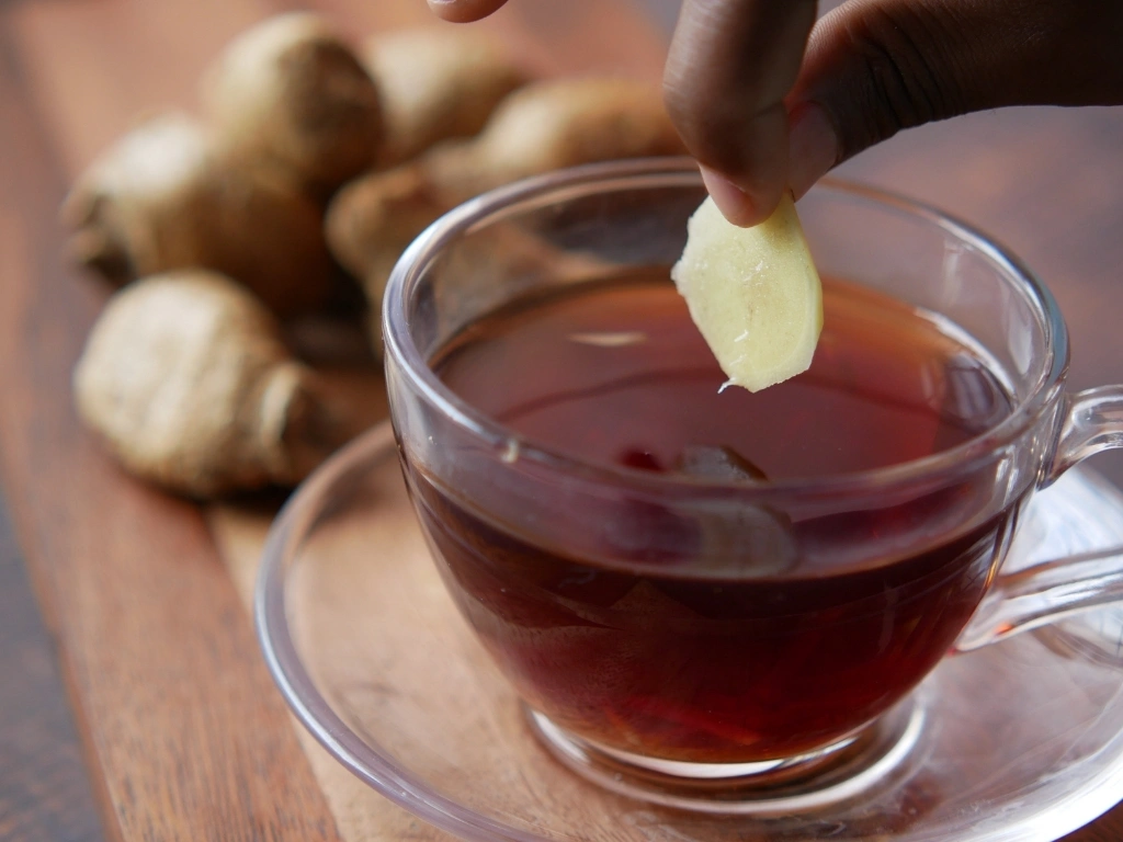 Person putting a slice of ginger into a cup of tea