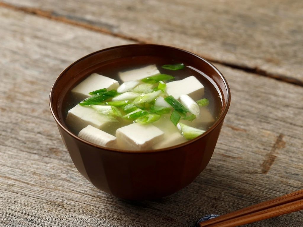 Small bowl of miso tofu soup on a wooden table, next to chopsticks