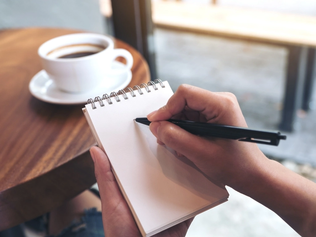 A person holding a pen over a blank notepad