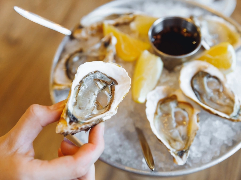 Fresh raw oysters on a half shell served on ice with lemon wedges and dipping sauce