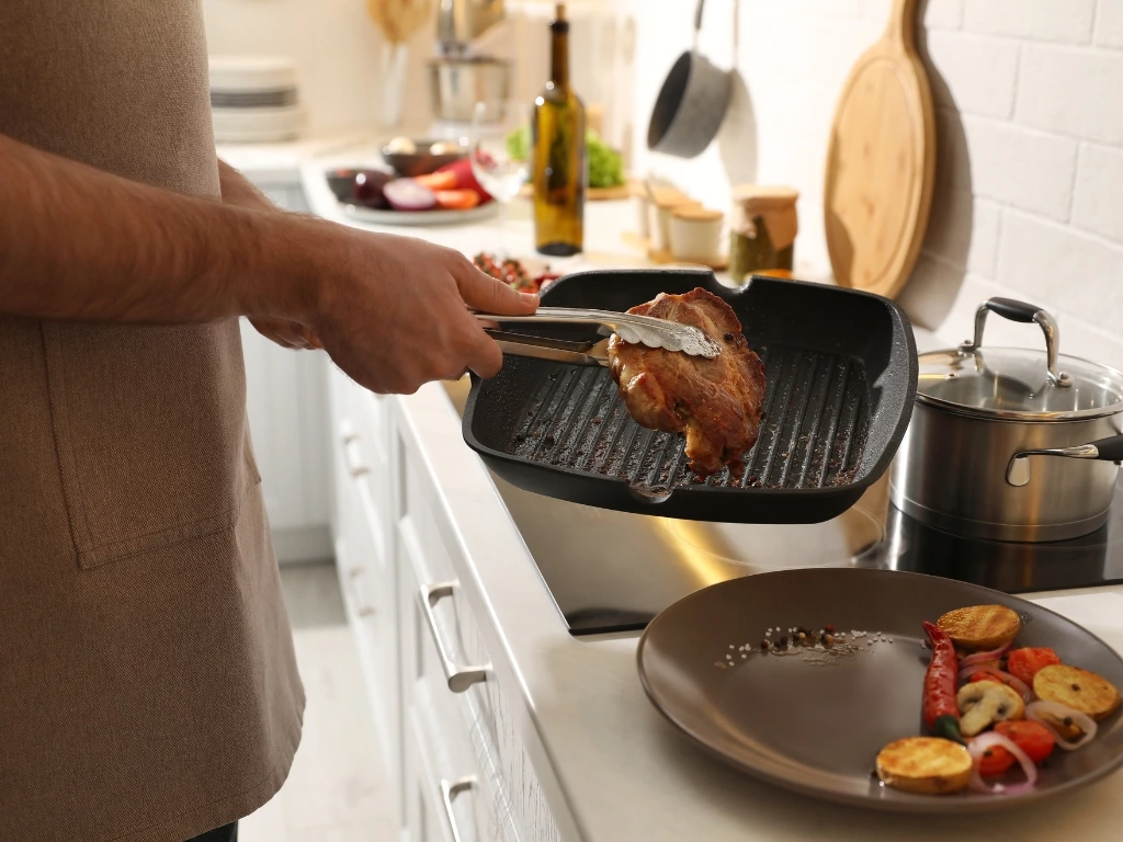 Man transferring a piece of chicken from a grill pan onto a brown plate with side vegetables