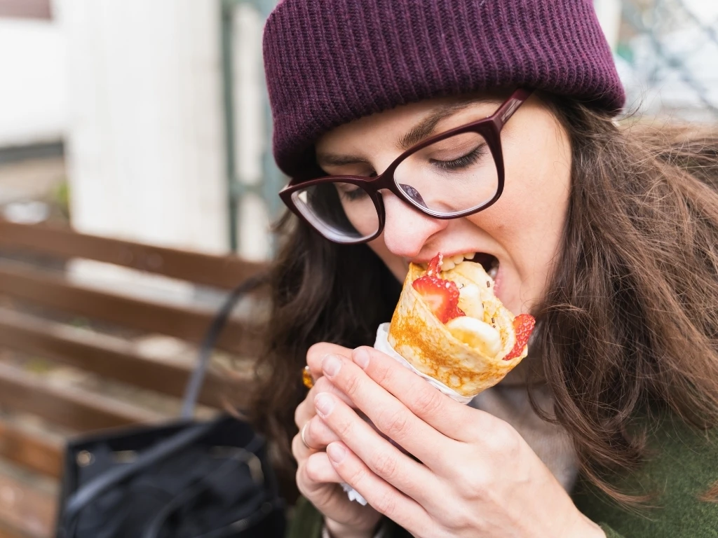 Woman eating fast street food, Take away sweet pancake big roll, banana, strawberry
