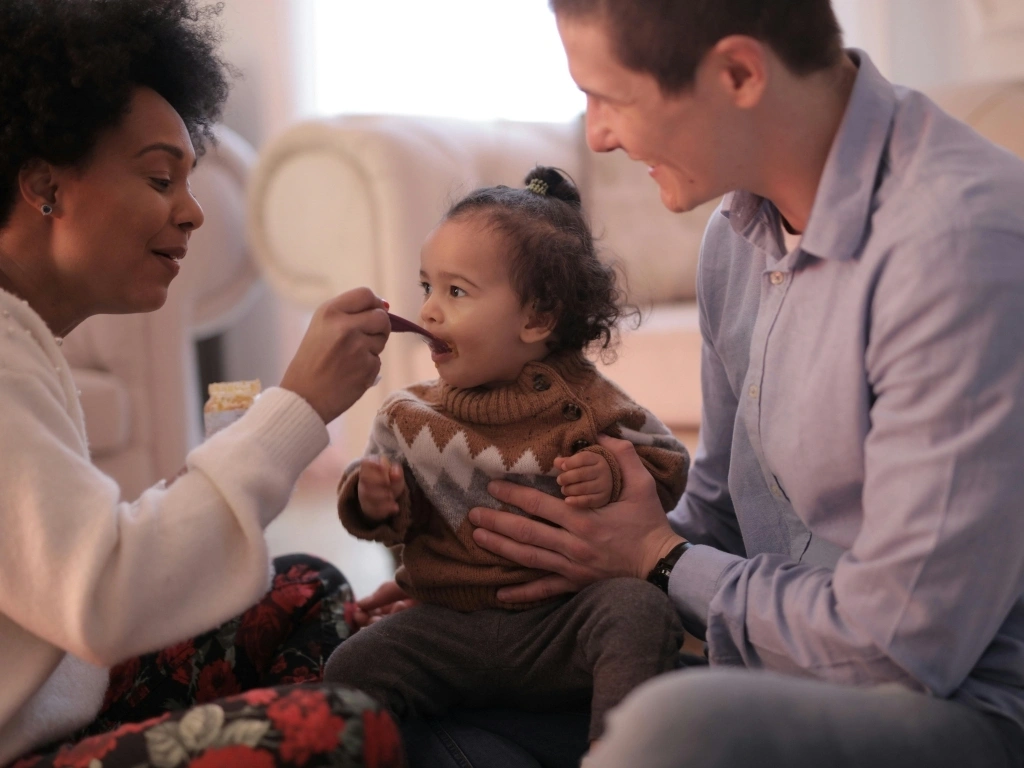 Woman feeding infant with peanut butter, while a man holds the child up