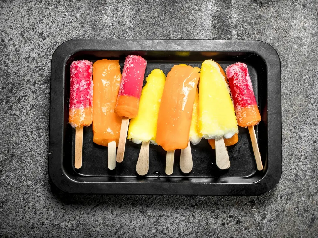 Different flavors of frozen fruit pops in a black tray