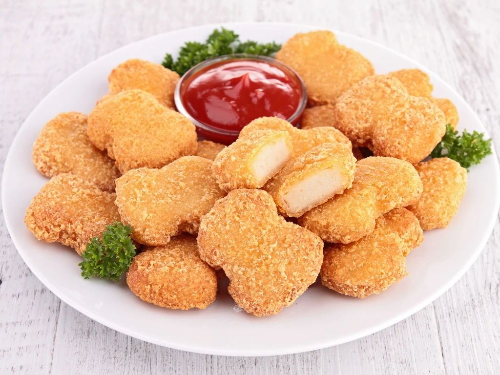Plate of fried chicken nuggets served with ketchup and greens