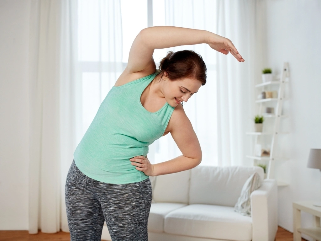 fitness, sport, exercising, training and lifestyle concept - smiling plus size woman stretching at home