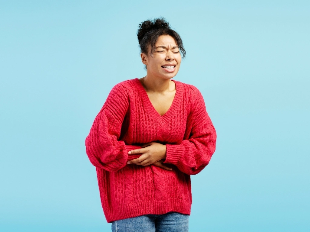 Young woman suffering from strong stomach ache on blue background