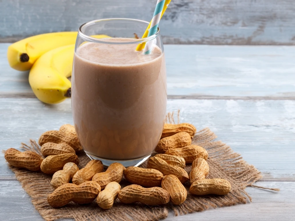 Glass of chocolate peanut butter banana shake, next to key ingredients