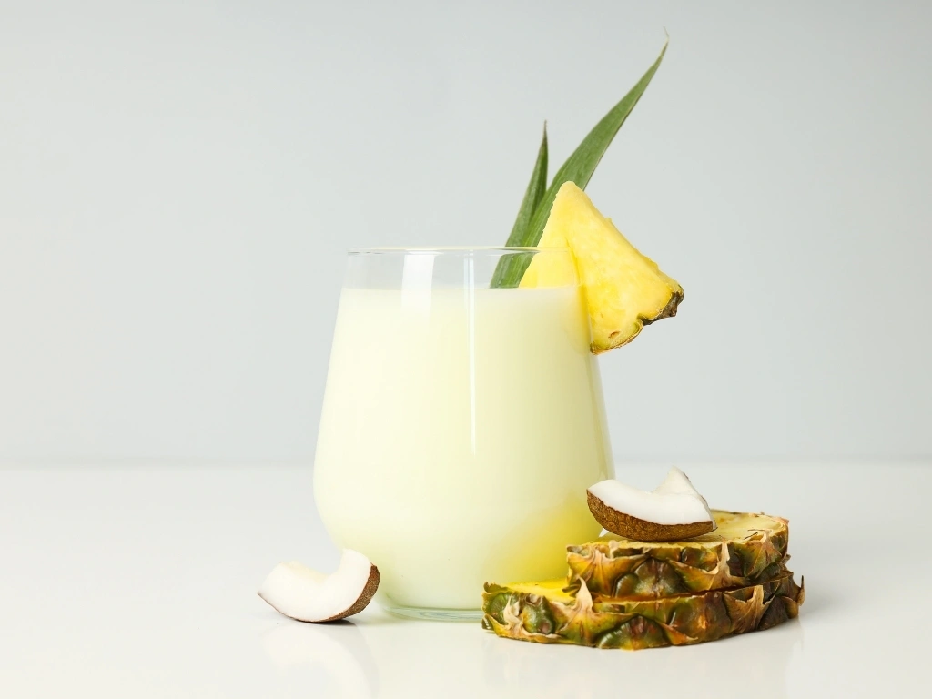Glass of tropical coconut protein shake, next to key ingredients