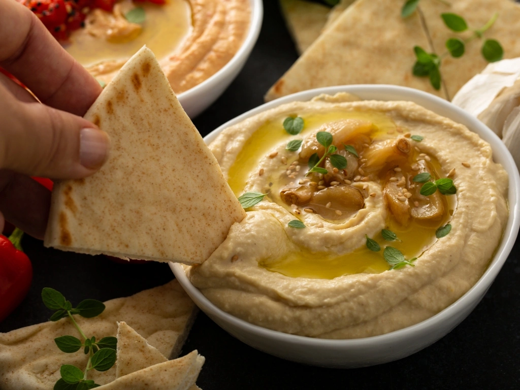 Person dipping pita bread in a bowl of hummus
