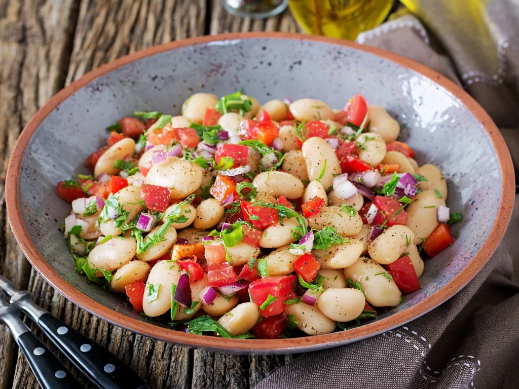 White bean salad tossed with diced tomatoes, red onions, and fresh herbs in a ceramic bowl