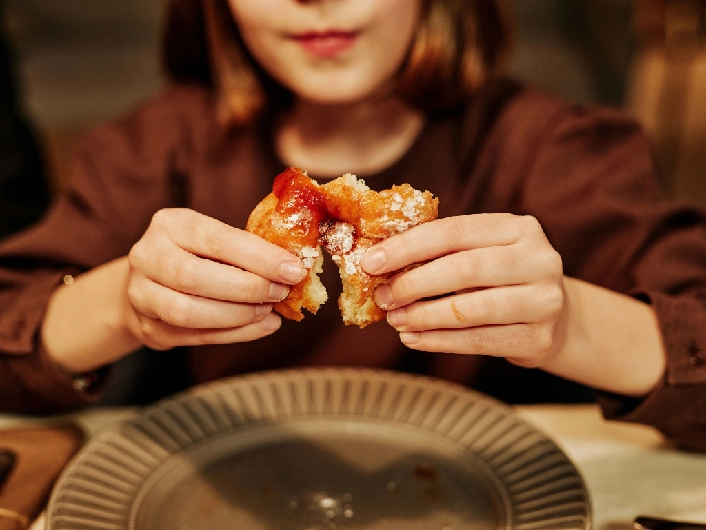 Woman breaking apart a piece of sugary donut with jam, holding it above a big grey plate