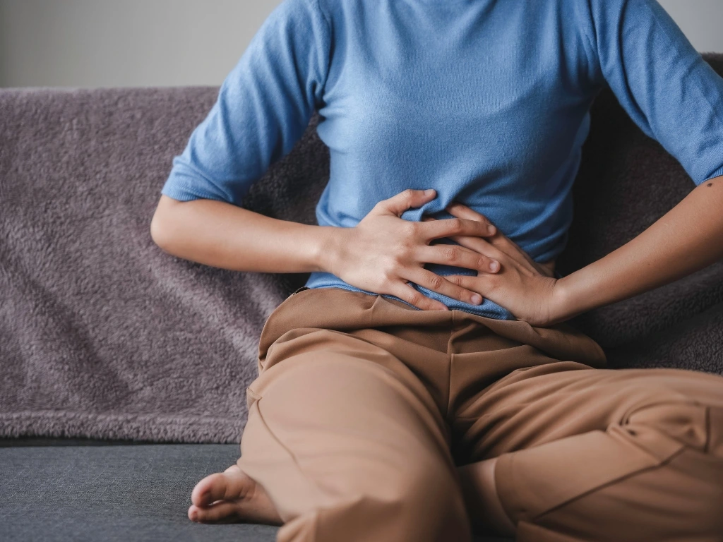 Person sitting on a couch holding their stomach with both hands in pain