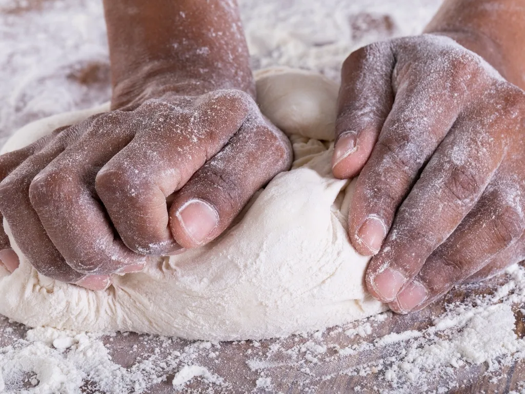 Close-up of flour-dusted hands kneading raw dough on a wooden surface