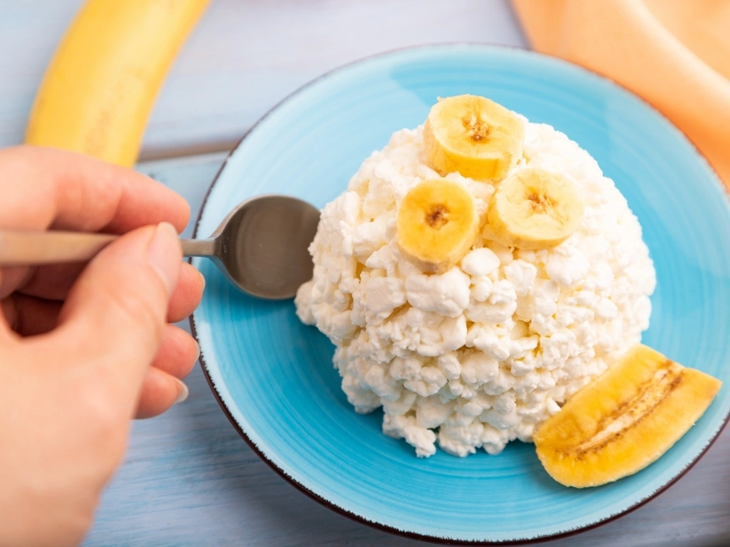 Person scooping some cottage cheese served with sliced banana