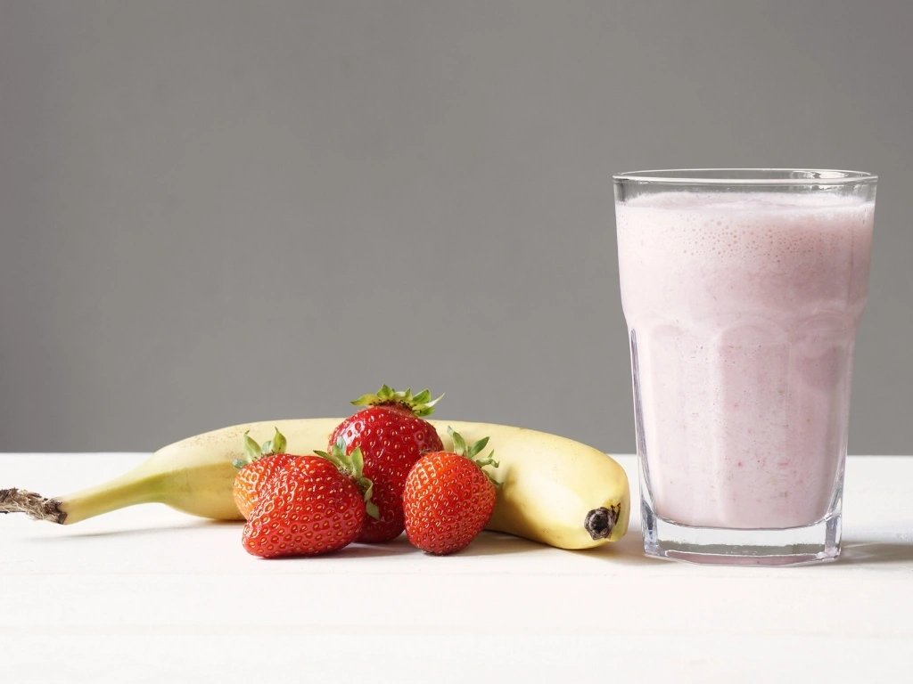 Glass of protein shake, next to some strawberries and a banana