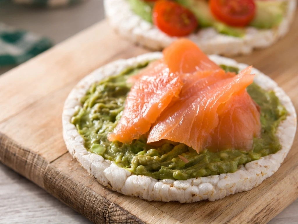 Salmon and avocado spread on puffed rice cake, served on a wooden board