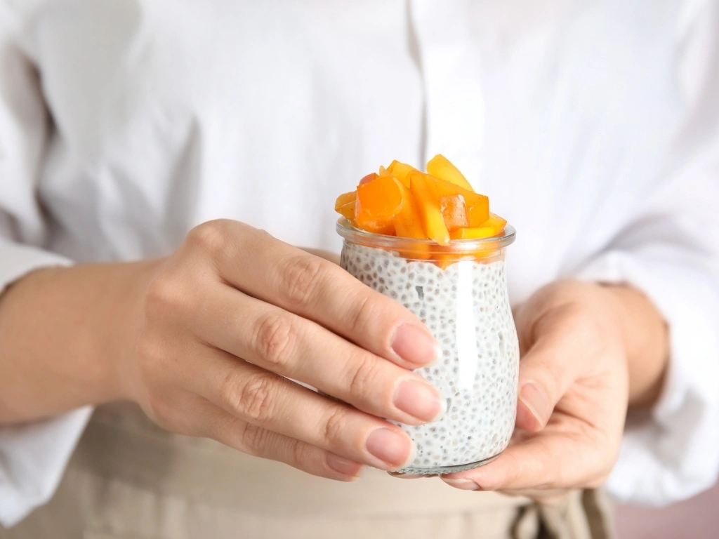 Person holding a jar of chia pudding topped with fruit