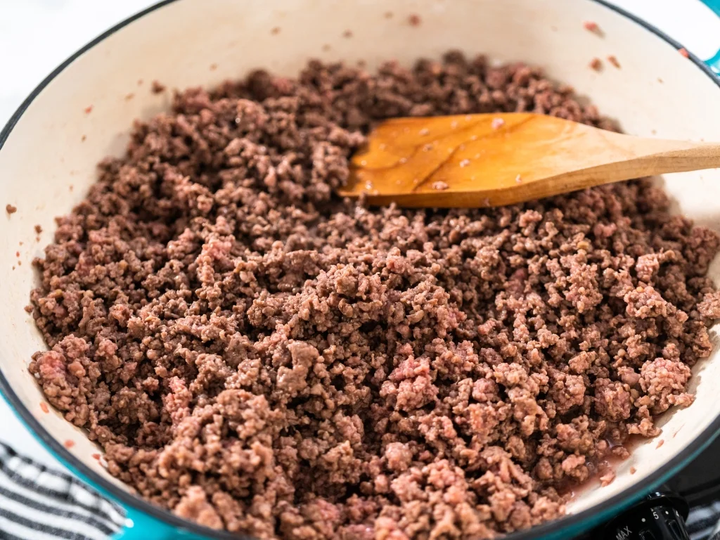 Ground beef cooked in a pan with a wooden spatula