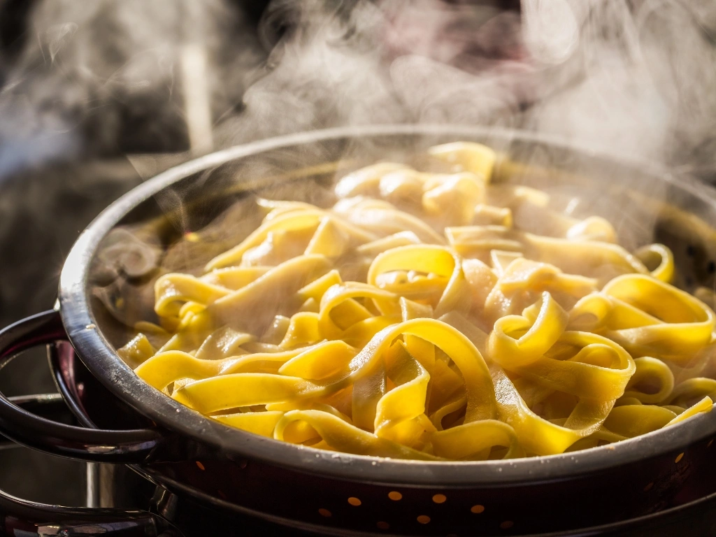 Freshly cooked pasta in a metal colander with visible steam