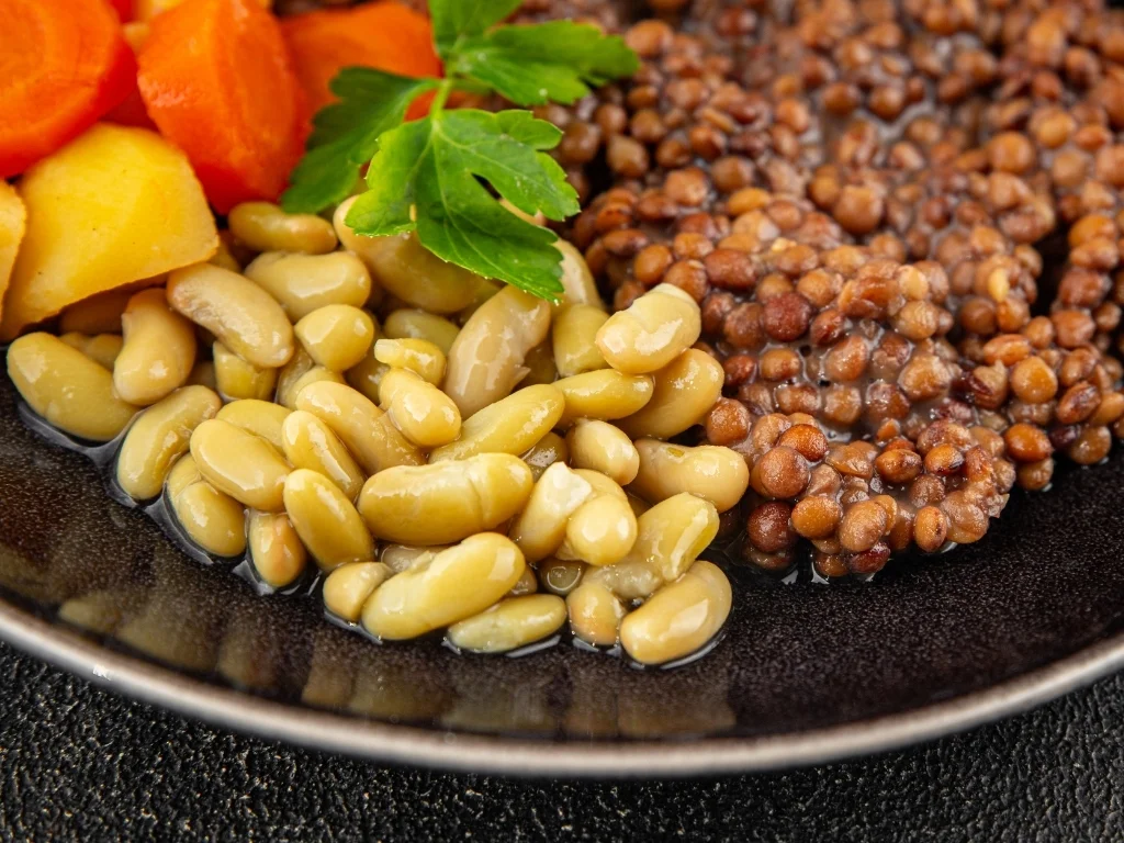 Brown lentils, white beans, carrots, and sweet potatoes on a black plate