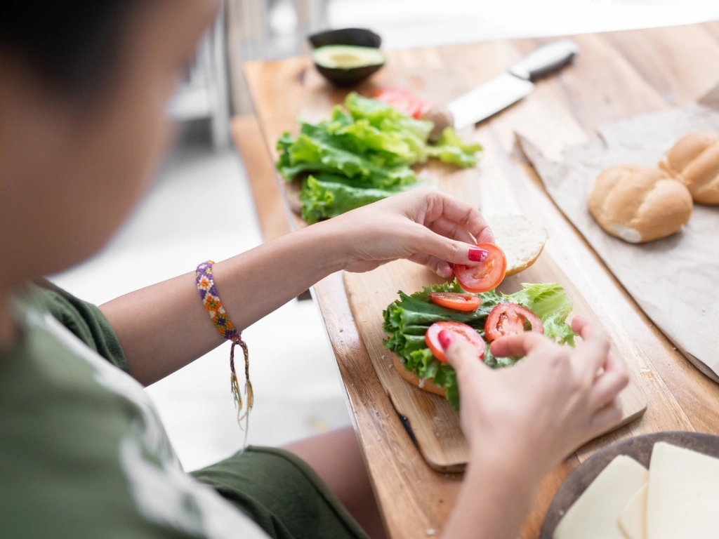 Woman adding tomato slices and lettuce to a sandwich