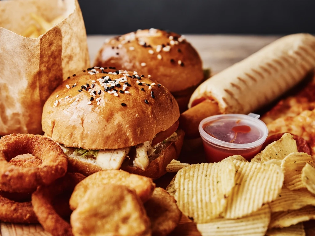 Spread of fast food including burgers, French fries, onion rings, potato chips, nuggets, and a hot dog