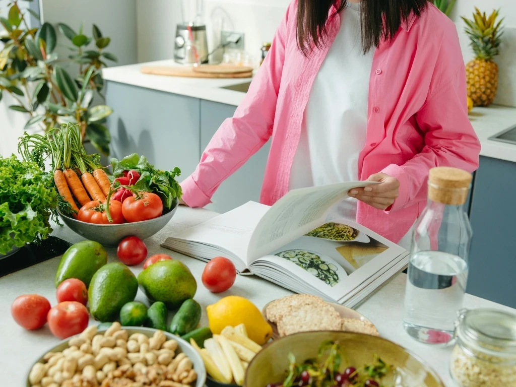 Woman reading a cookbook with a variety of ingredients on the kitchen countertop