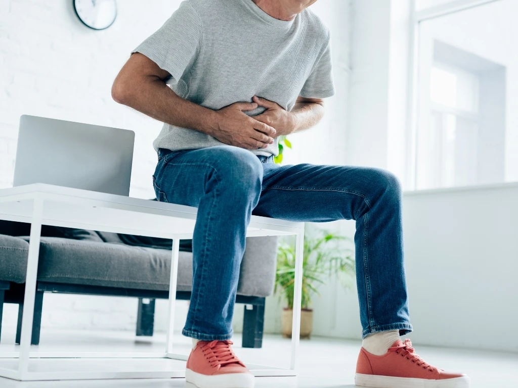Man sitting on a coffee table, clutching his abdomen in discomfort