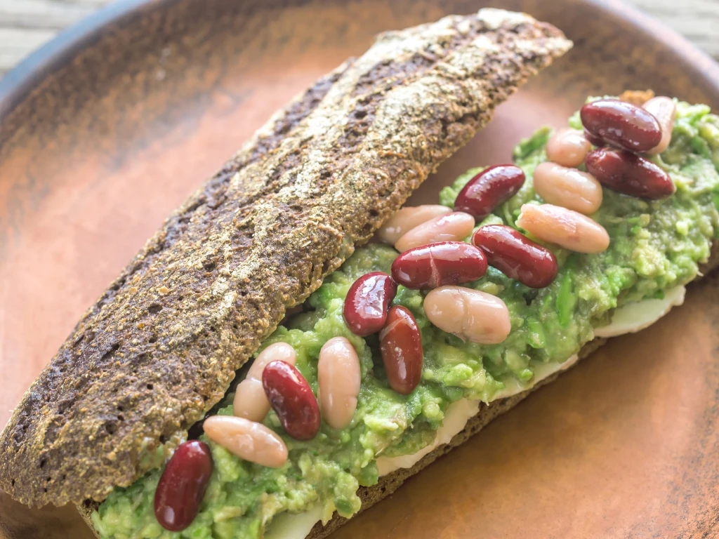 Beans, tofu, and avocado on whole-grain toast, served on a brown plate