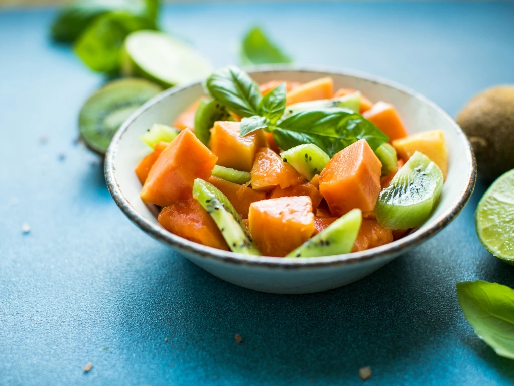 Bowl of diced cantaloupe melon and sliced kiwi fruit salad garnished with fresh basil leaves
