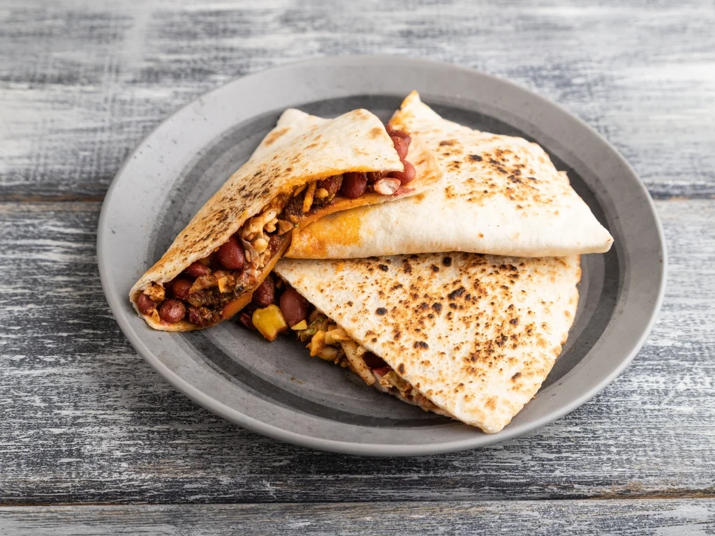 Grey plate of toasted quesadilla triangles filled with red beans, melted vegan cheese, and sweet corn kernels
