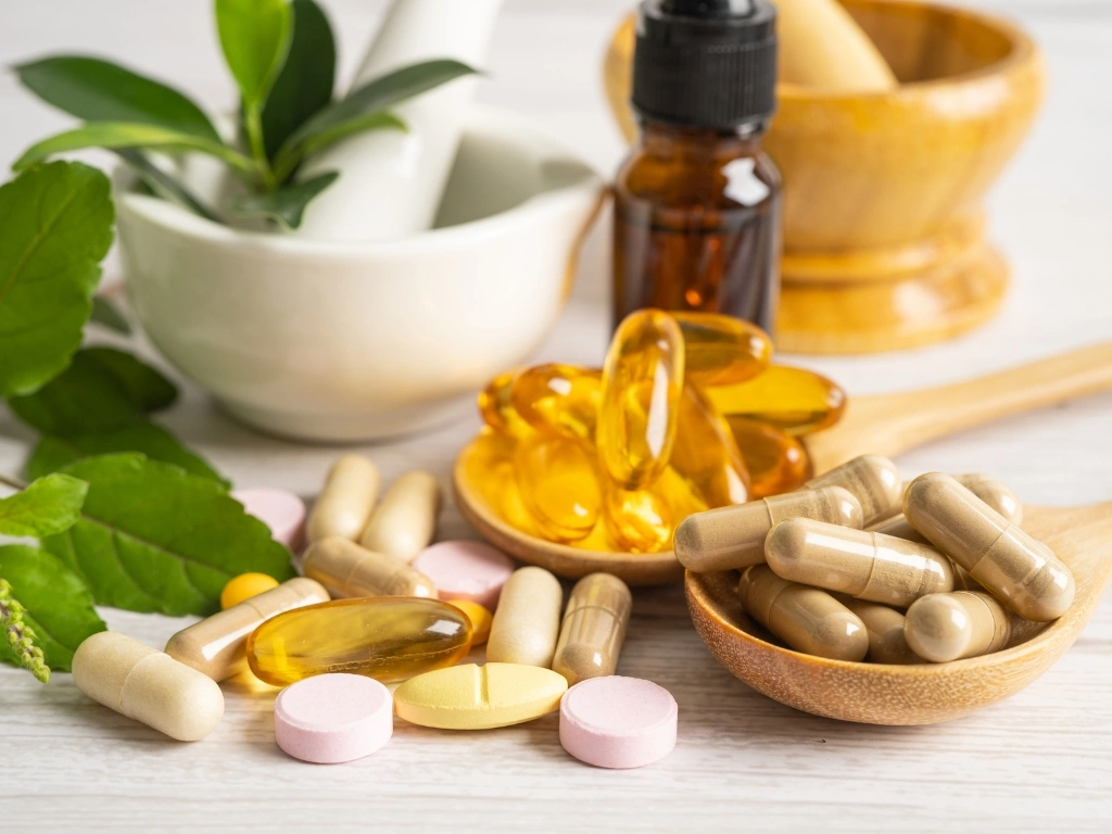 An assortment of tablets and capsules, with bowls, wooden spoons, and leaves in the background