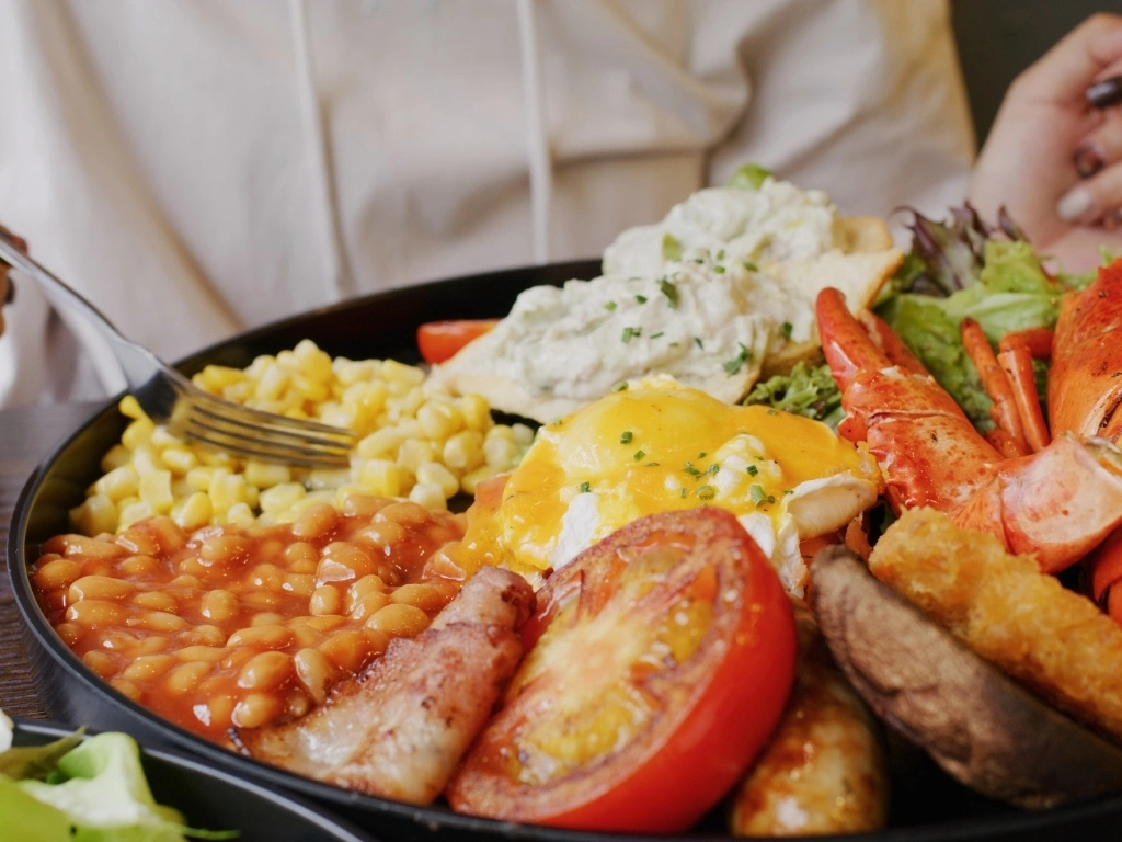 A person eating a plate of food with beans, seafood, corn, salad, and eggs
