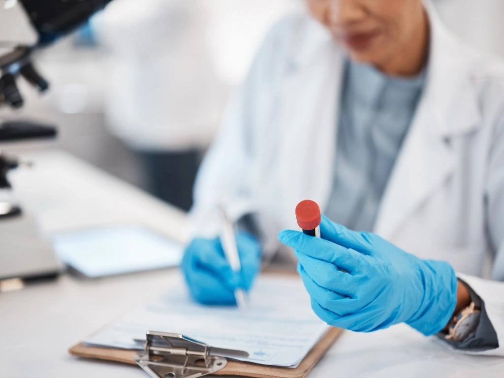 Laboratory technician inspecting a vial, writing down observations on a notepad